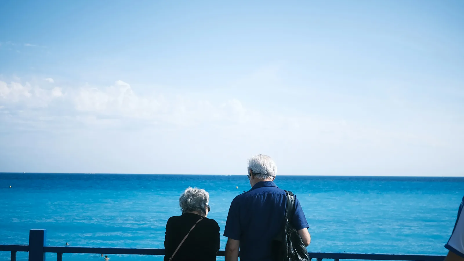 An older couple standing at a railing, looking out at the ocean